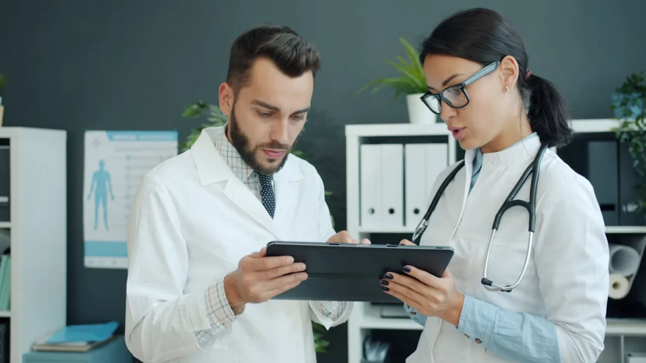 Two healthcare professionals reviewing information on a tablet in a clinic.