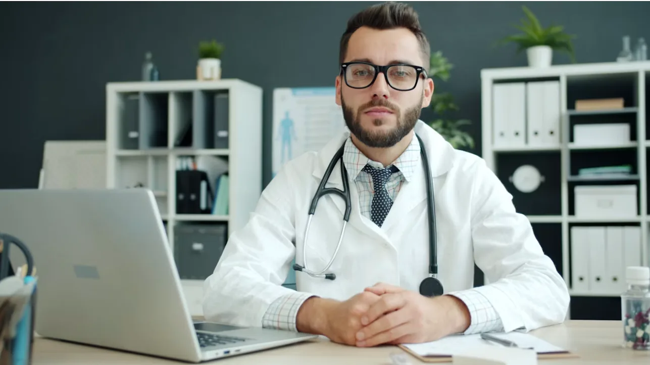 A healthcare professional seated at a desk with a laptop in a clinic office.