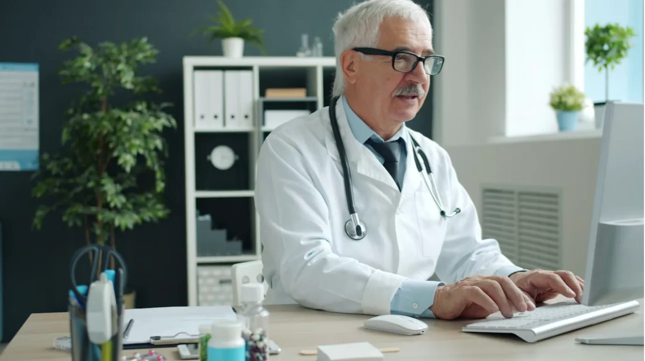 A healthcare professional working at a computer in a clinic office.