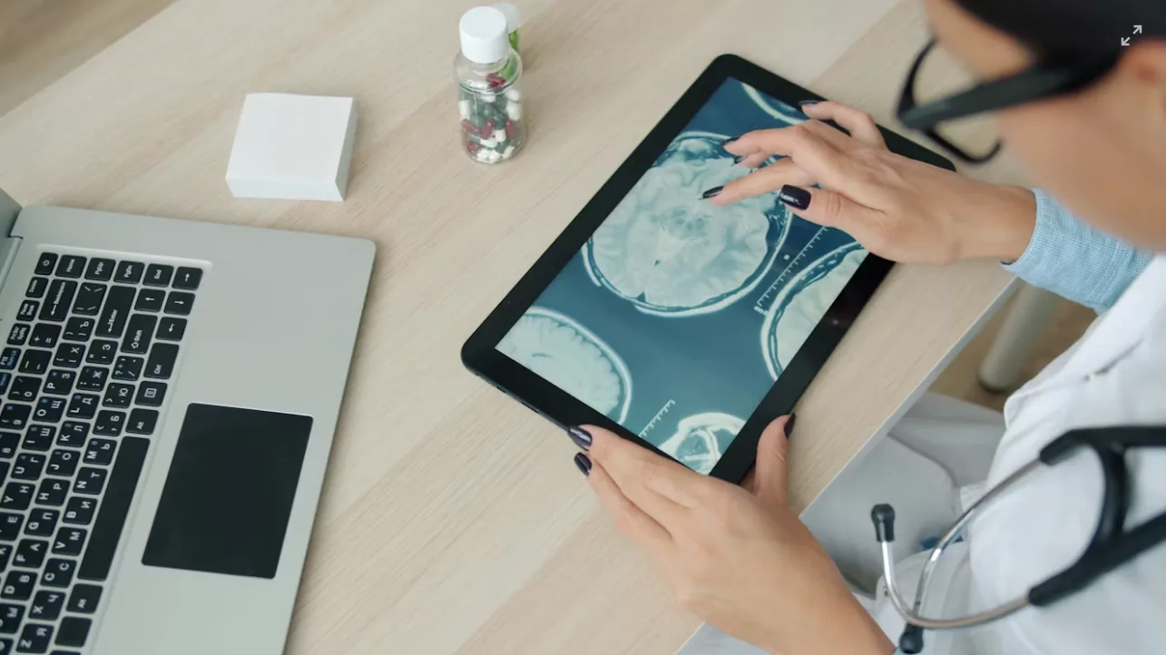 A clinician reviewing medical scans on a tablet beside a laptop.